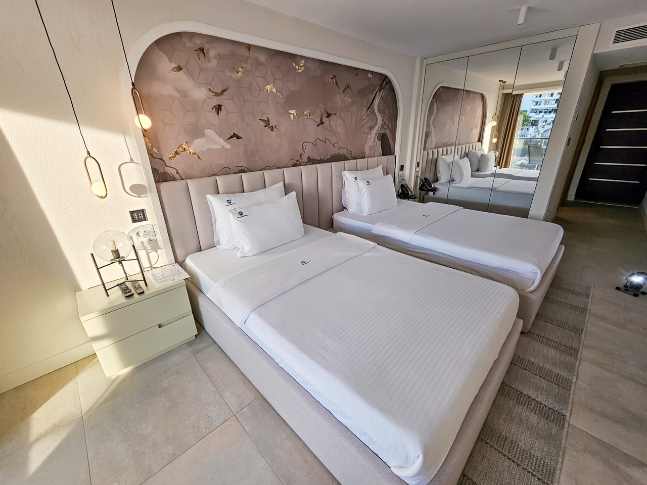 Moderna hotelska soba sa dva kreveta, elegantnom taupe glavnom naslonjaÄu sa zlatnim pticama i ogledalom