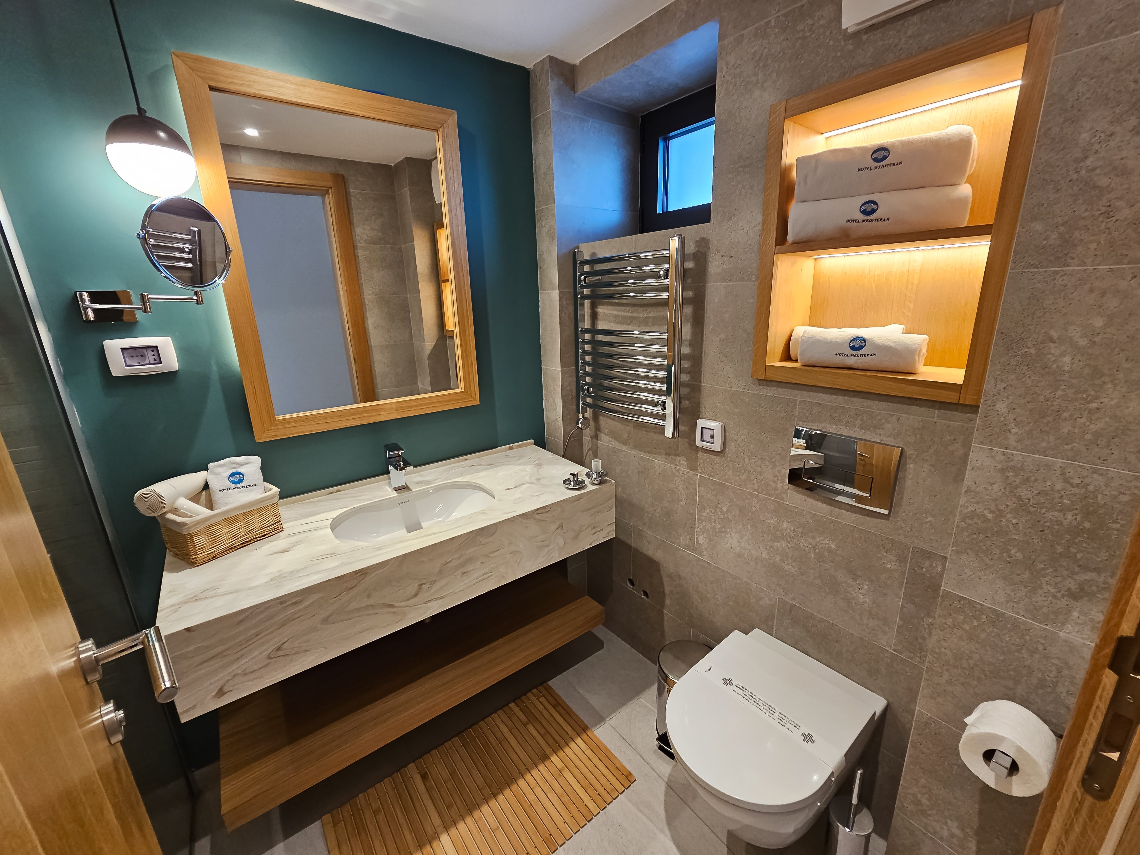 Moderan hotelski kupatilo sa tirkiznom akcentnom zidnom, mramornim umivaorom i osvetljenim nicama sa peÅ¡kiri